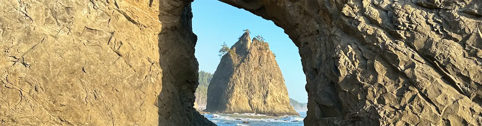 A sea stack seen through a natural rock arch at Rialto Beach in Olympic National Park