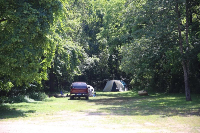 A car and tent occupy a campsite surrounded by trees.