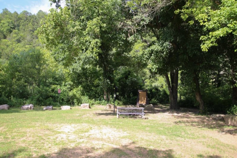 A sunny campsite with a picnic table, lantern post, and fire ring.