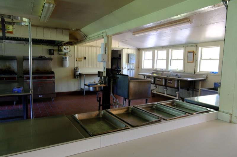 Commercial kitchen with stainless steel counters, warming bins, gas stoves and ovens and sinks
