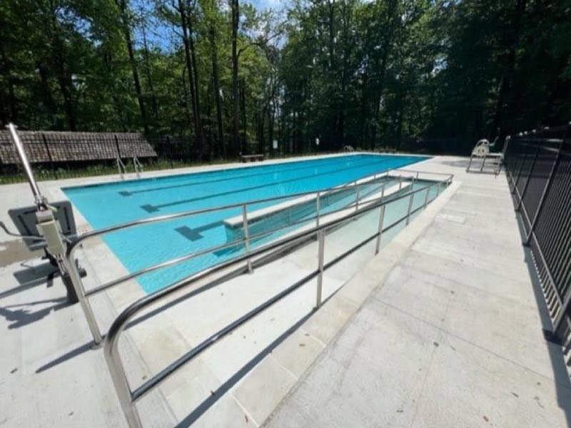 Bright blue pool surrounded by cement with a ramp and lift for accessibility.