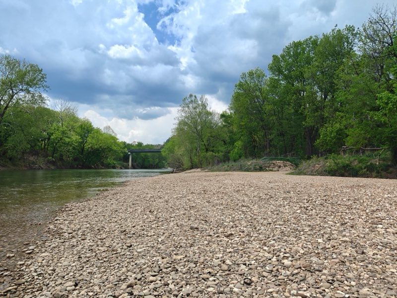A wide, rocky riverbank stretches across the foreground, covered in small, rounded pebbles.