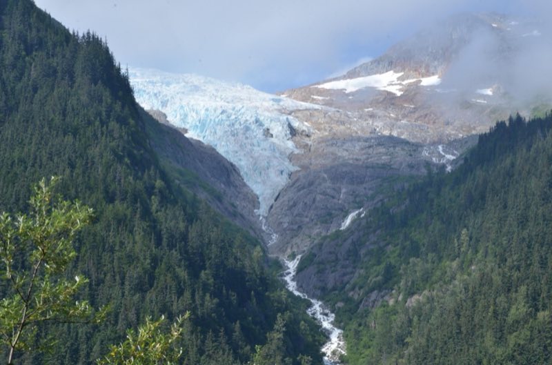 Glacier nestled in mountains and clouds with a waterfall at the bottom