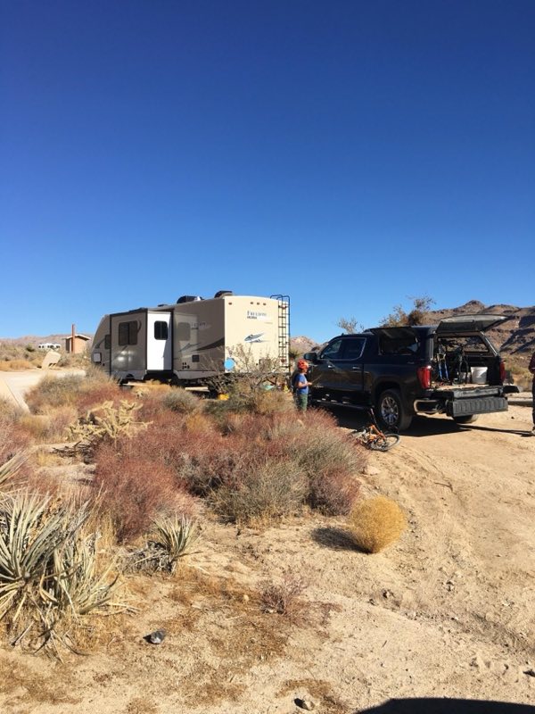A large RV and truck are pulled into a campsite. A small child with his back turned is in the front