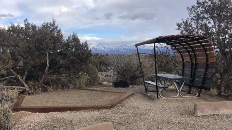 A tent pad and covered picnic table with a background of Sleeping Ute mountain range's snow-covered peaks.
