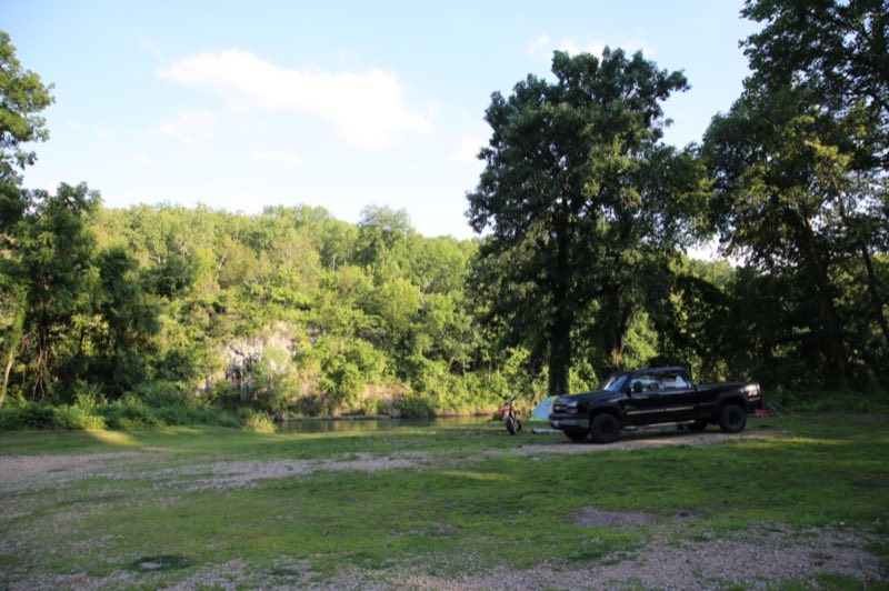 A tent and pickup truck occupy a campsite near the river's edge.