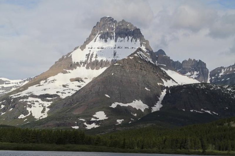 craggy topped mountain rises above forest and lakeshore