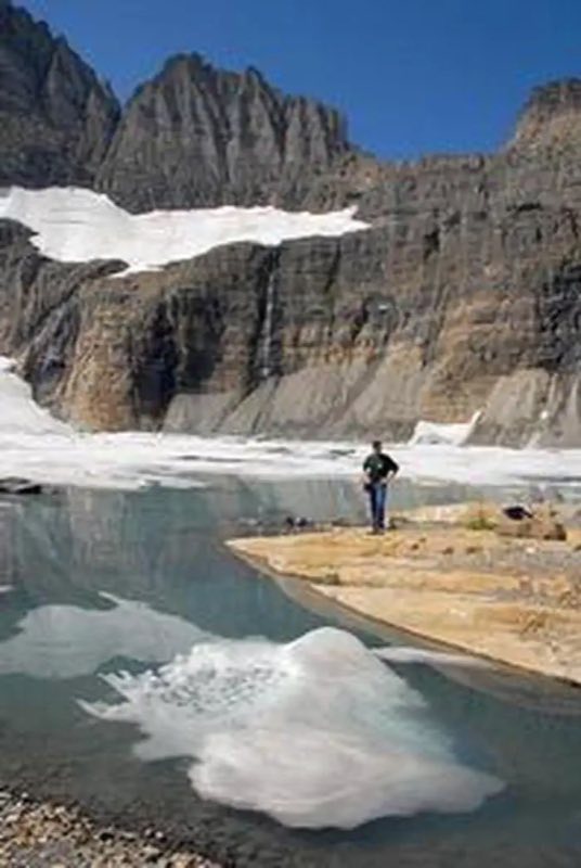 A man views rock cliffs above an alpine lake