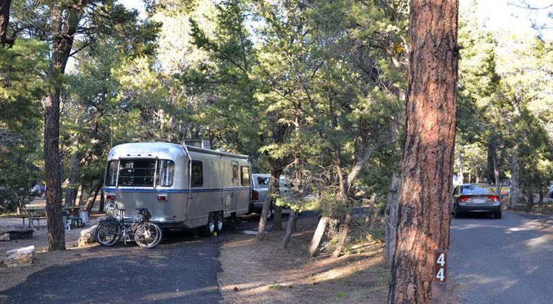 Image: a truck with an attached trailer is parked in a paved pull-through campsite. Two bi