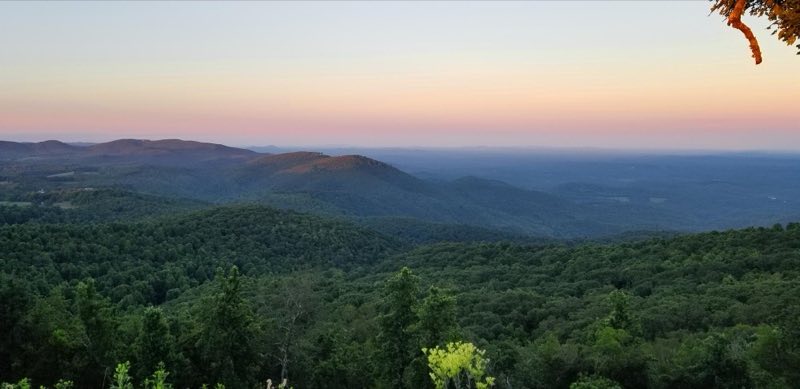 Green forests cloak mountains beneath a yellow and red morning sky