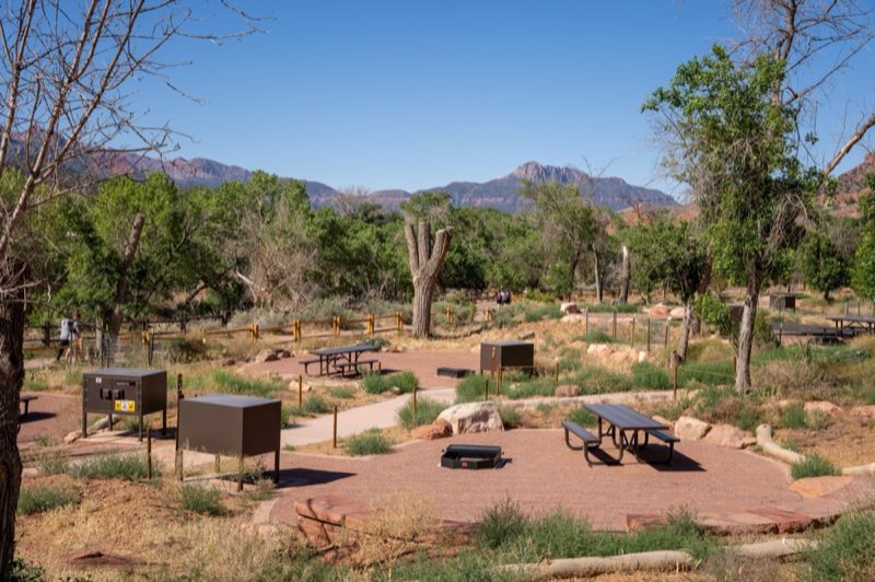 A grassy campground with flat, gravel sites and a nearby paved pathway.