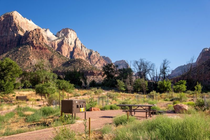 Flat, gravel campsites are spread along a grassy slope with basic amenities.