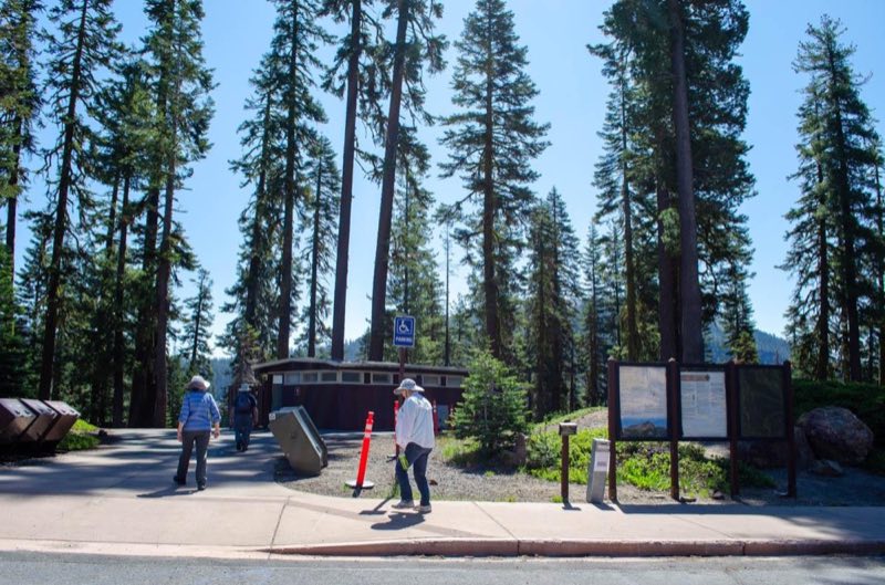 Two people walk along a paved pathway toward a small brown building.