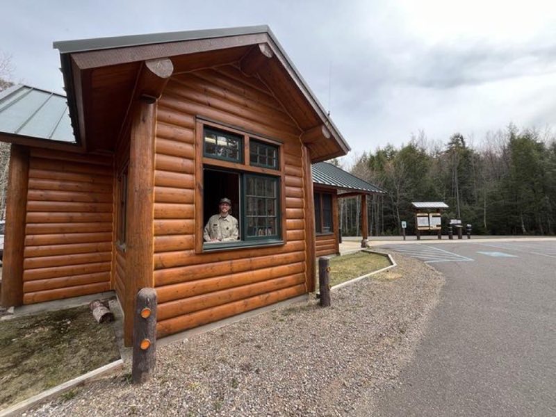 A window is open on a log entrance station building with a staff member inside ready to greet visitors.