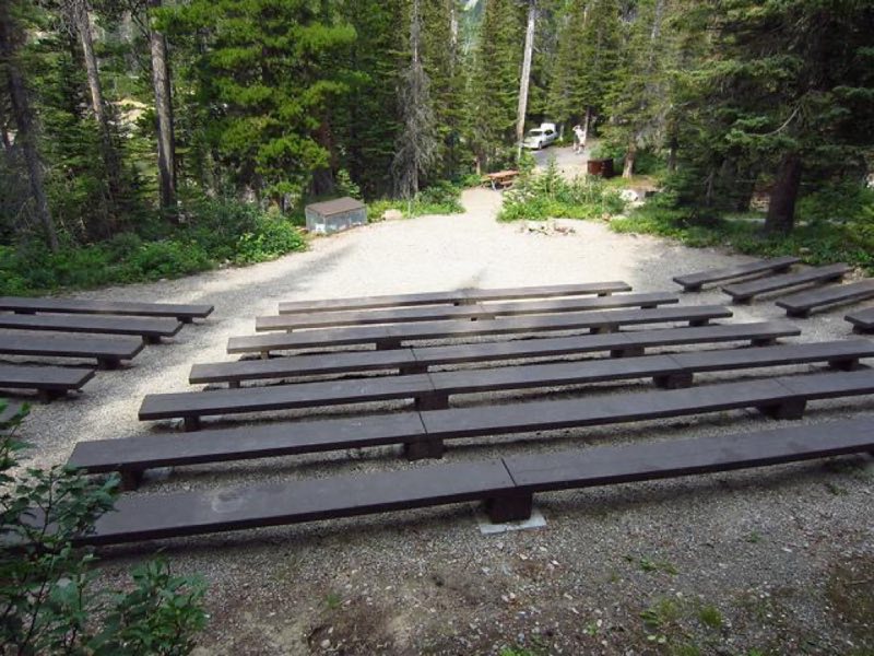 long wooden benches in gravel clearing with picnic table and food storage box in background