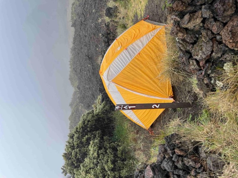 orange tent on gravel surface behind brown stake reading 1 and 2